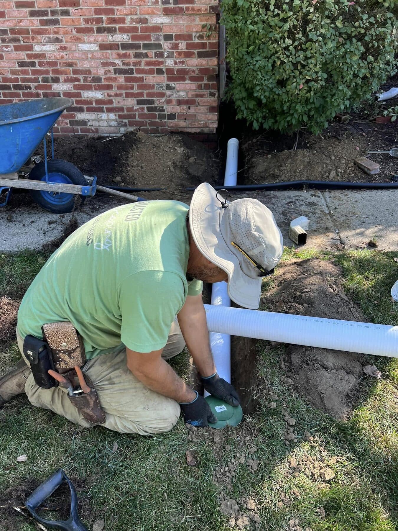 Crew connecting a downspout to buried solid drain pipe beside a brick house