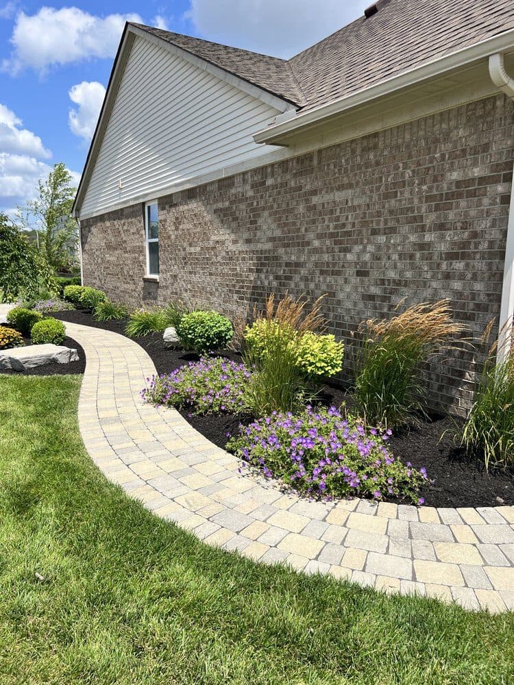 Curved paver path through new planting beds with ornamental grasses and boulders, installed by Trusted Landscaping